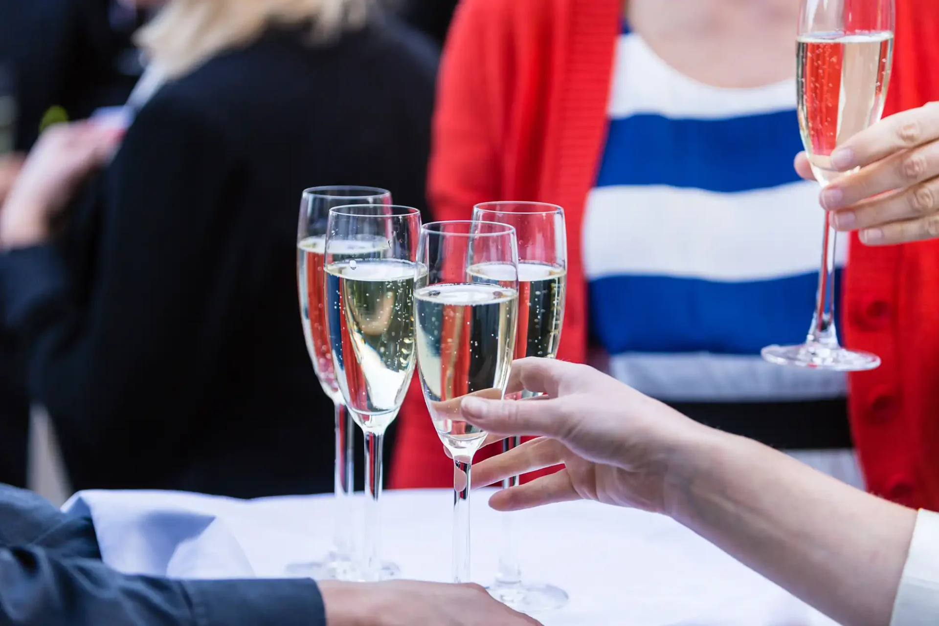 People toasting with champagne glasses at a social event, with a focus on the glasses clinking together.