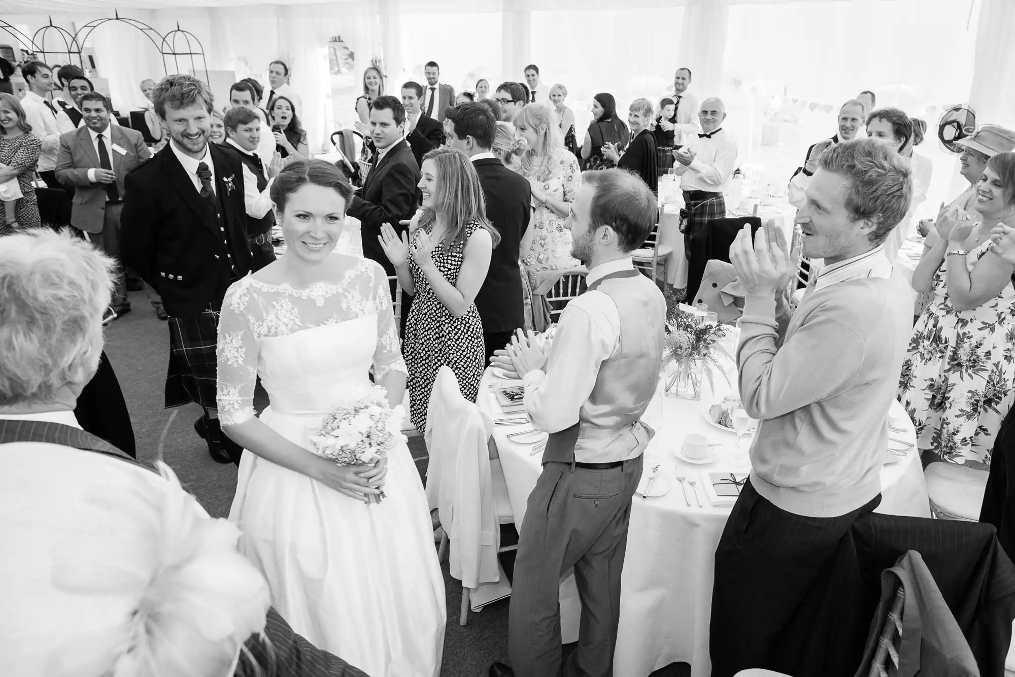 Bride and groom walking through a cheering crowd inside a tent at their wedding reception.