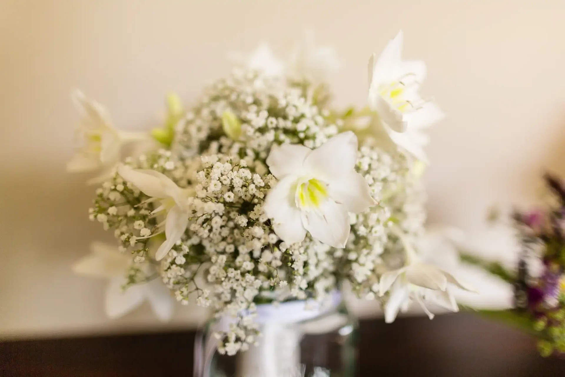 A close-up of a bouquet featuring white daffodils and baby's breath in a glass vase on a wooden surface.