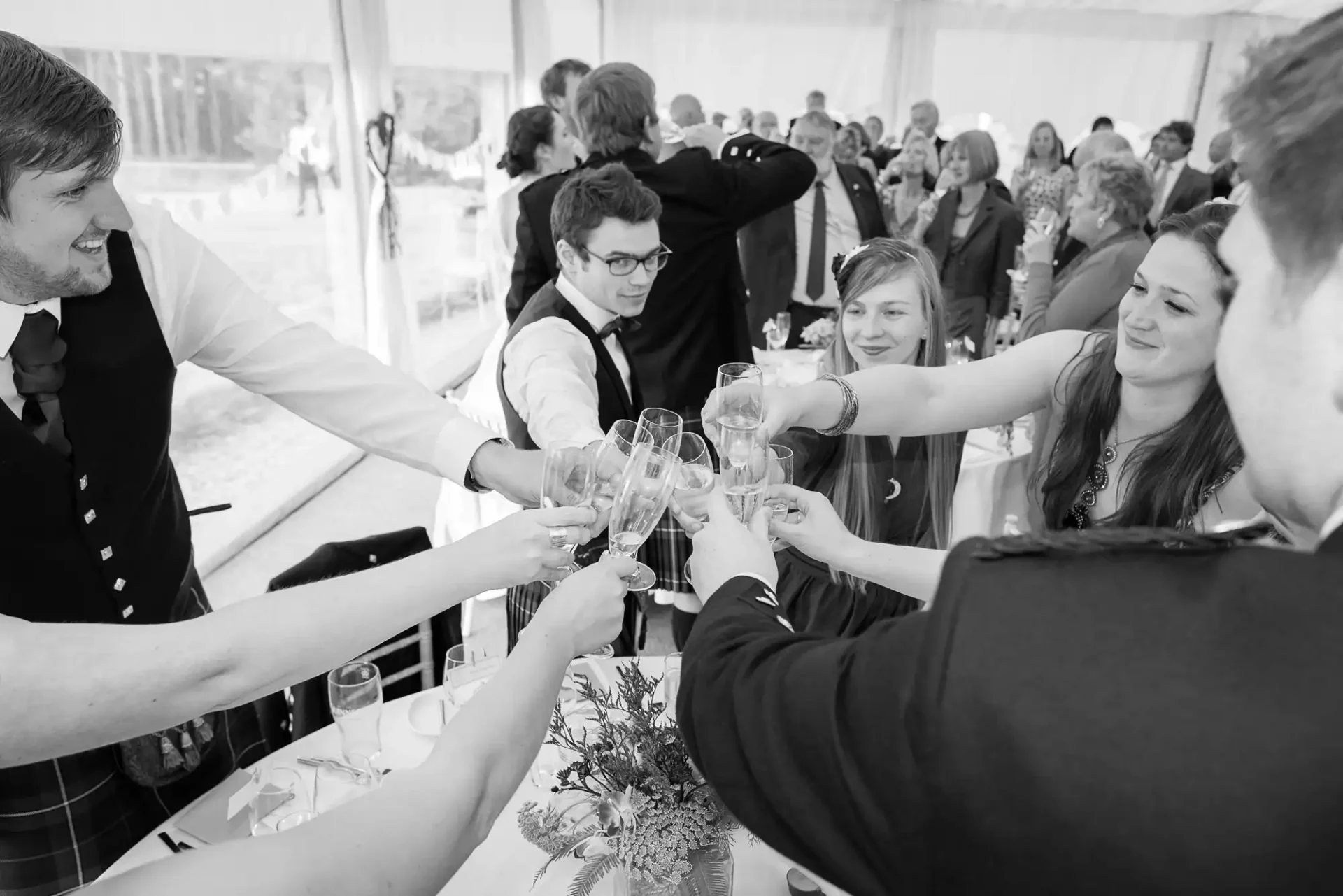 A group of people in formal attire making a toast with wine glasses at a festive gathering inside a tent.