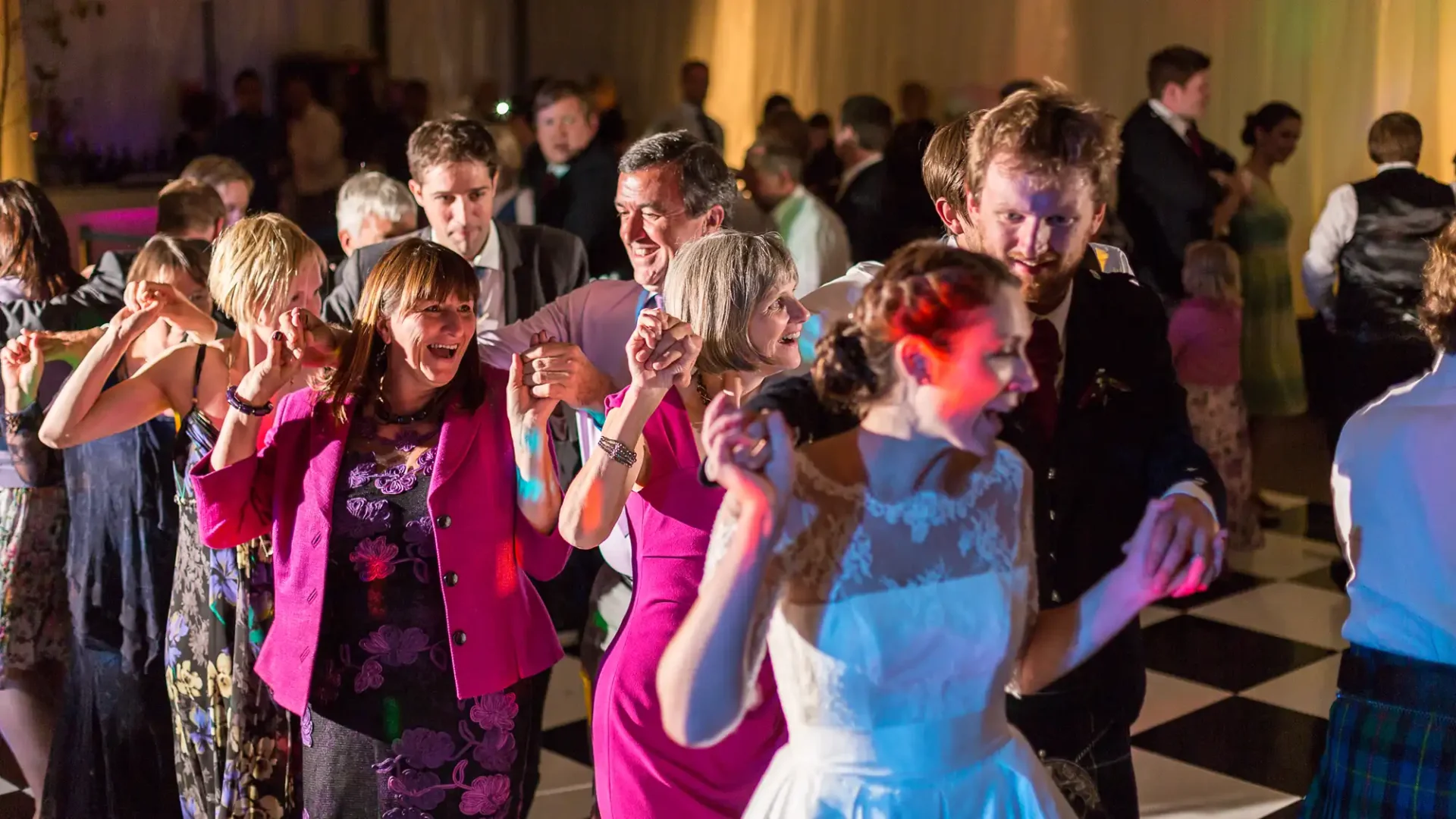 Guests dancing joyfully at a wedding reception, with a focus on a diverse group of adults in evening attire.
