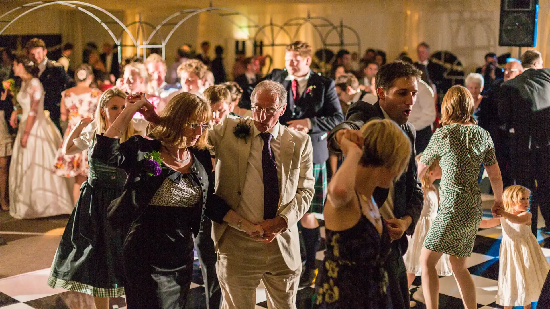 Guests dancing at a lively evening wedding reception, with various couples and individuals of different ages interacting on the dance floor.