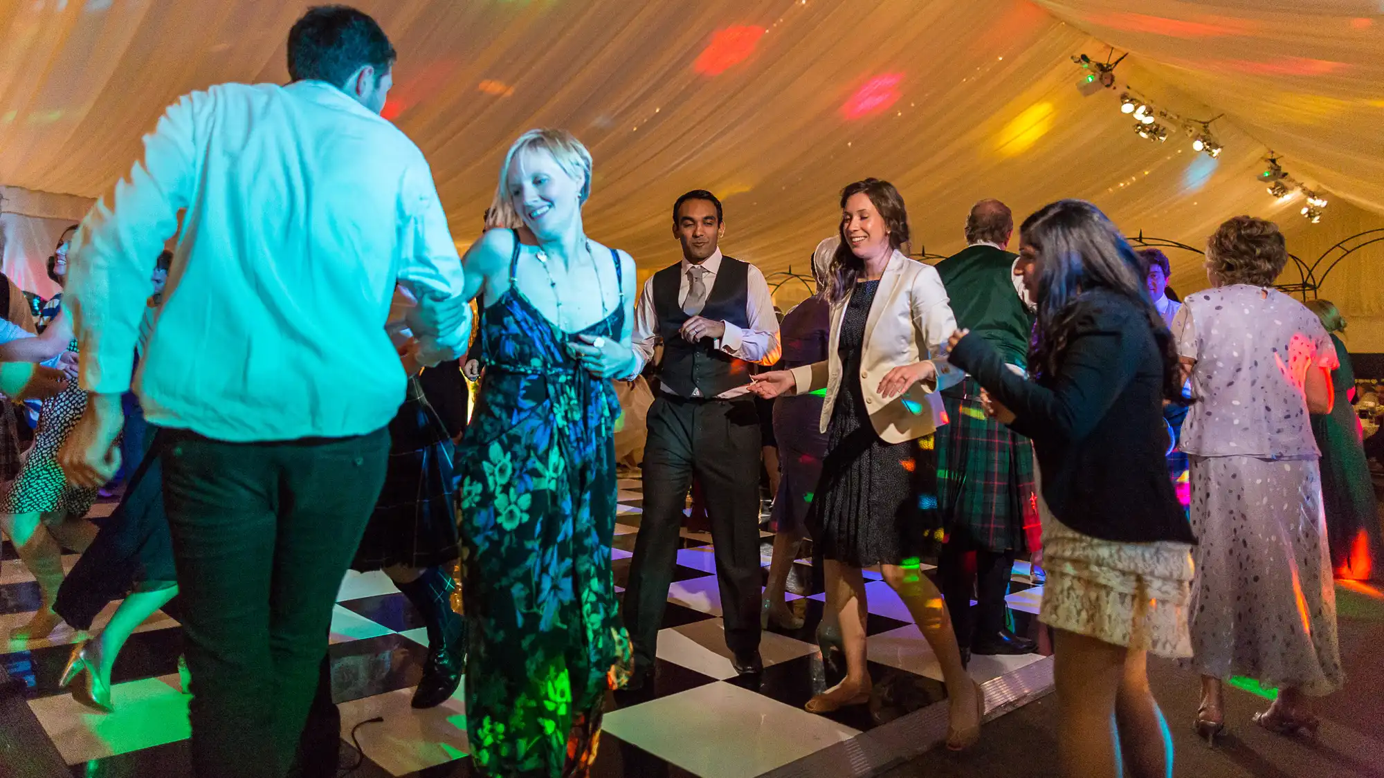 People dancing joyfully in a tent with colorful lights at a festive event.