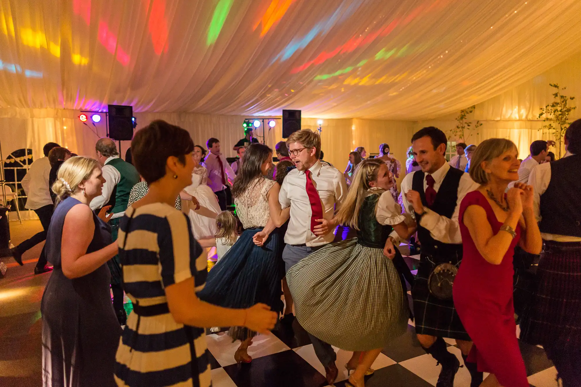 People dancing joyfully at a lively indoor party with colorful lights illuminating a tented venue.