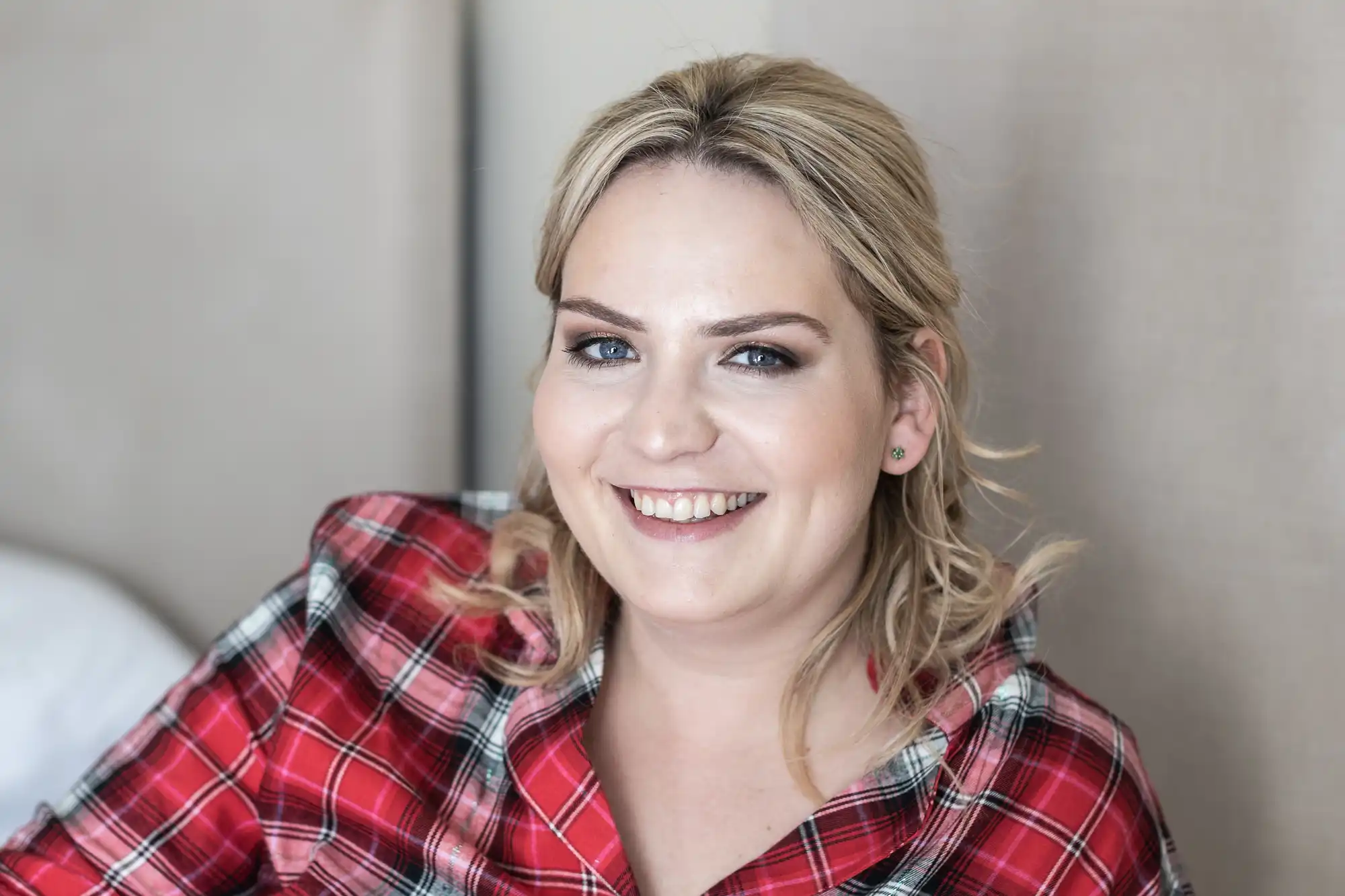 A person with blonde hair wearing a red plaid shirt smiles while looking at the camera.