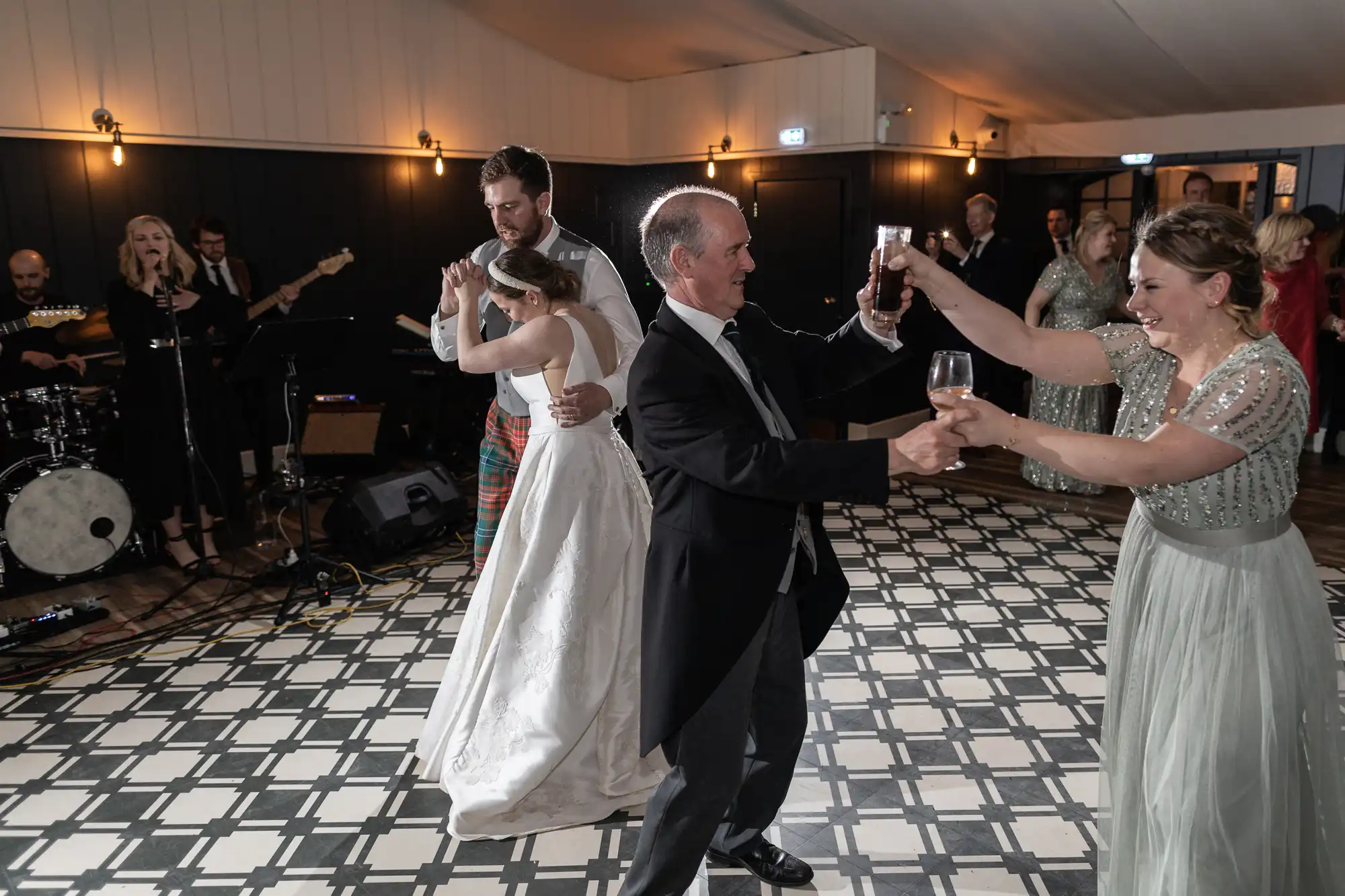 Guests are dancing at a wedding reception while a band performs in the background. The bride and groom are dancing together in formal attire.