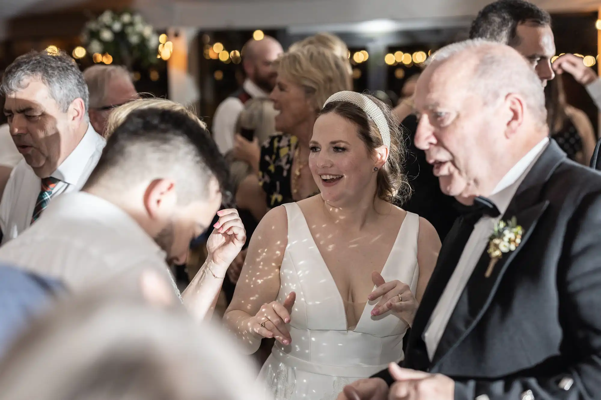 A bride and guests are dancing in a well-lit, crowded room during a wedding reception.