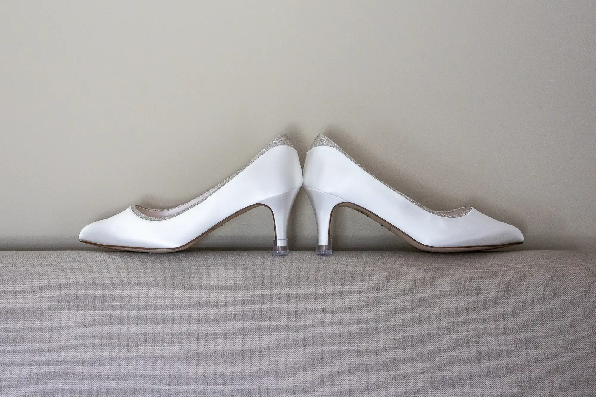 A pair of white high-heeled shoes are placed back-to-back against a gray background.