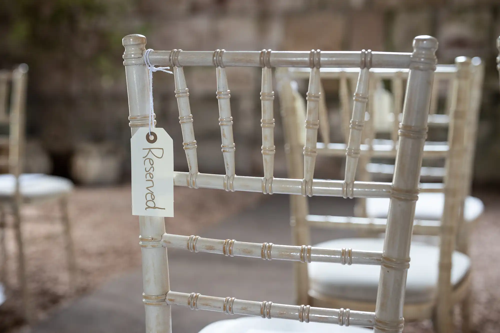 White chair with a "Reserved" tag hanging on its backrest, arranged in an outdoor setting.