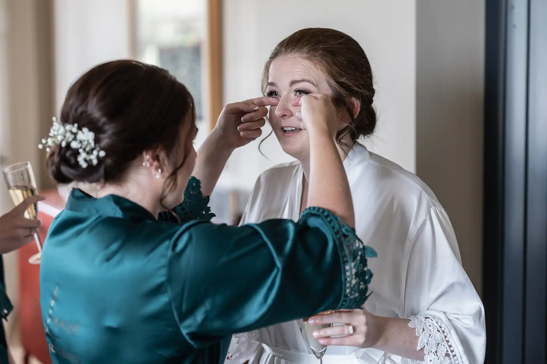 documentary style wedding photography example: Two women dressed in robes are seen in an emotional moment; one is wiping tears from the other's face in a comforting manner.