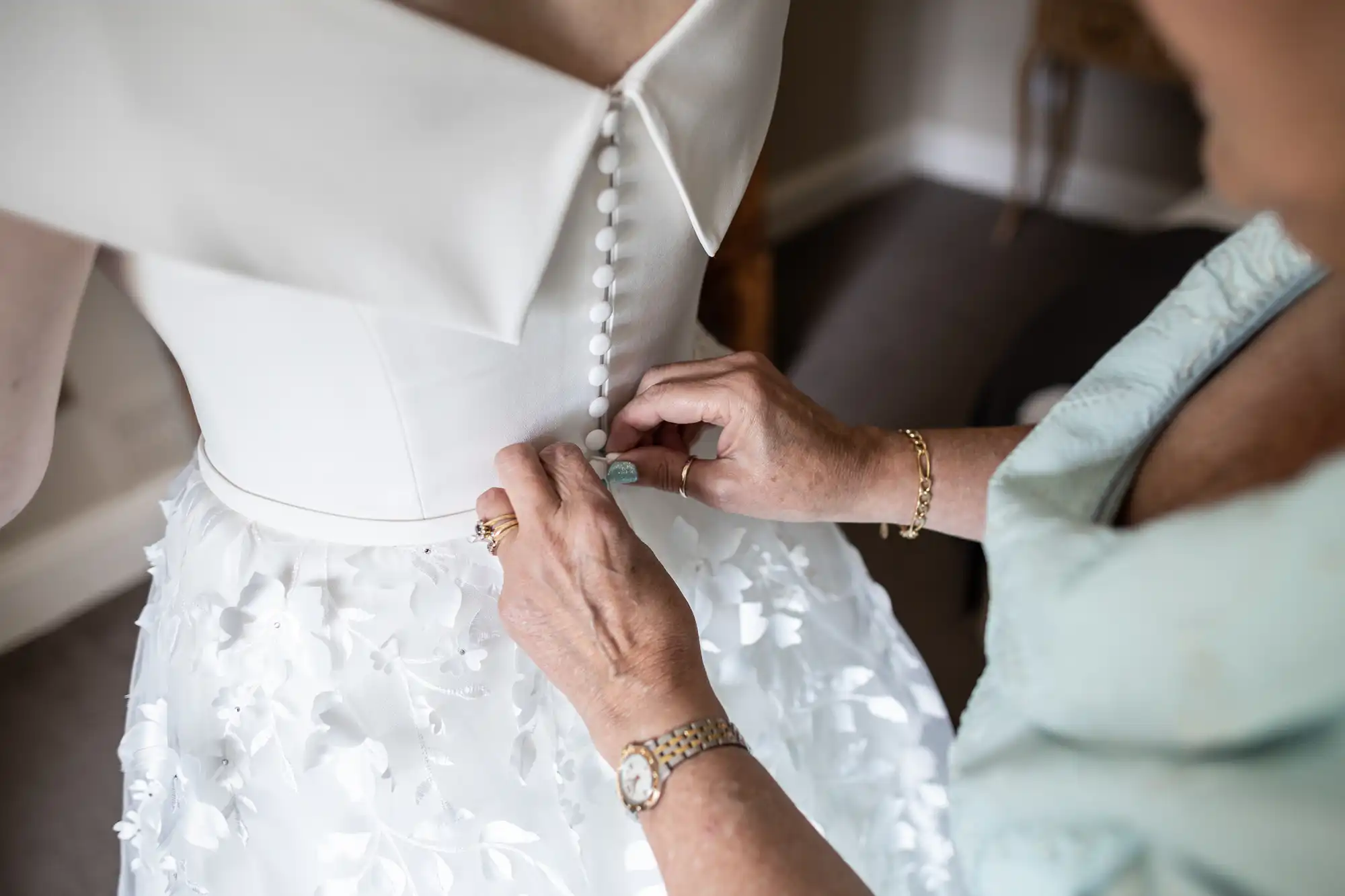 A close-up shot of a person in a white wedding dress being buttoned up by another person.