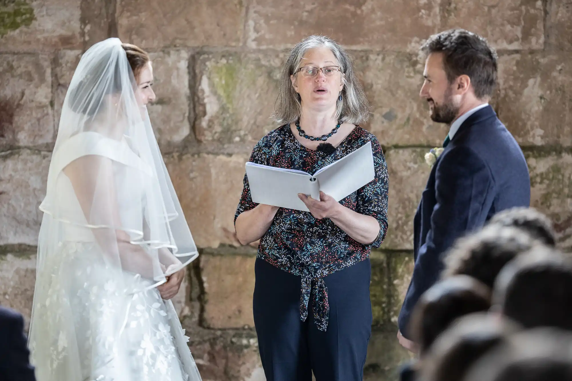 A bride and groom stand at the altar facing each other with an officiant reading from a book between them during their wedding ceremony.