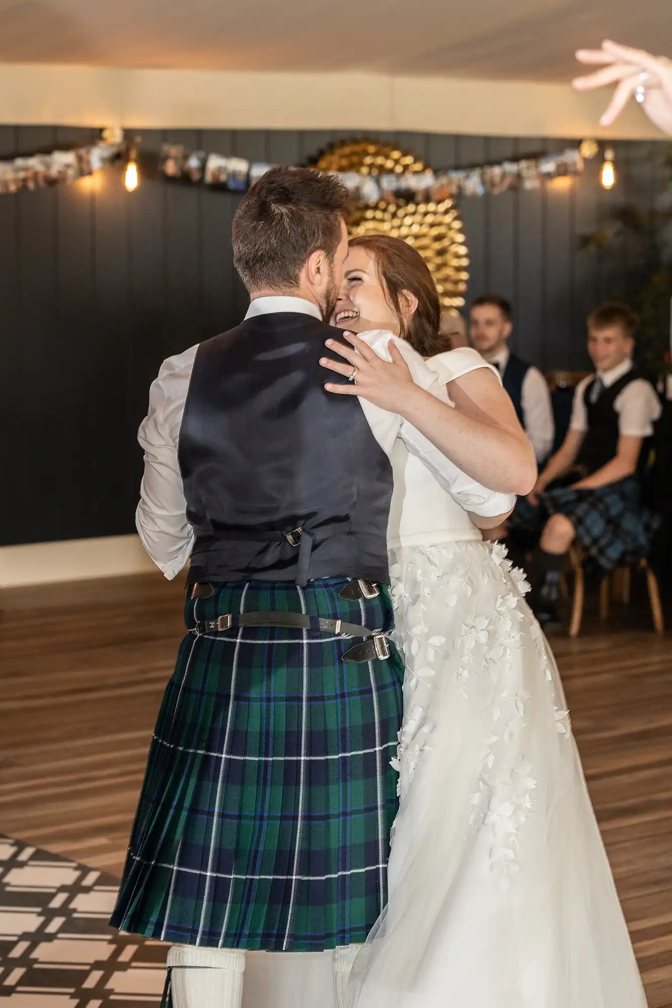 wedding at Dunglass Estate - a bride and groom dance closely together at their wedding reception. The groom wears a kilt, and the bride has an ornate white dress. A few seated guests are visible in the background.