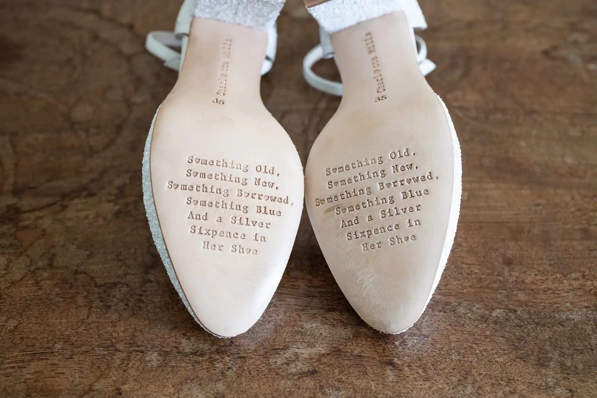 The image shows the soles of a pair of shoes with the traditional wedding rhyme: "Something Old, Something New, Something Borrowed, Something Blue, And a Silver Sixpence in Her Shoe" engraved on them.