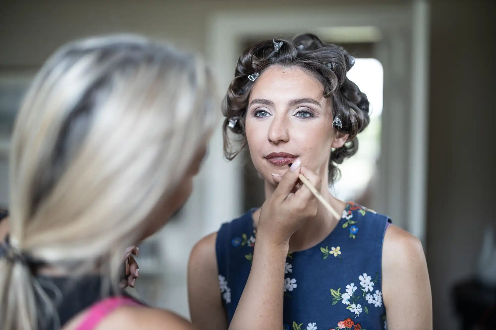 A woman with curled hair is having her makeup done by another woman.