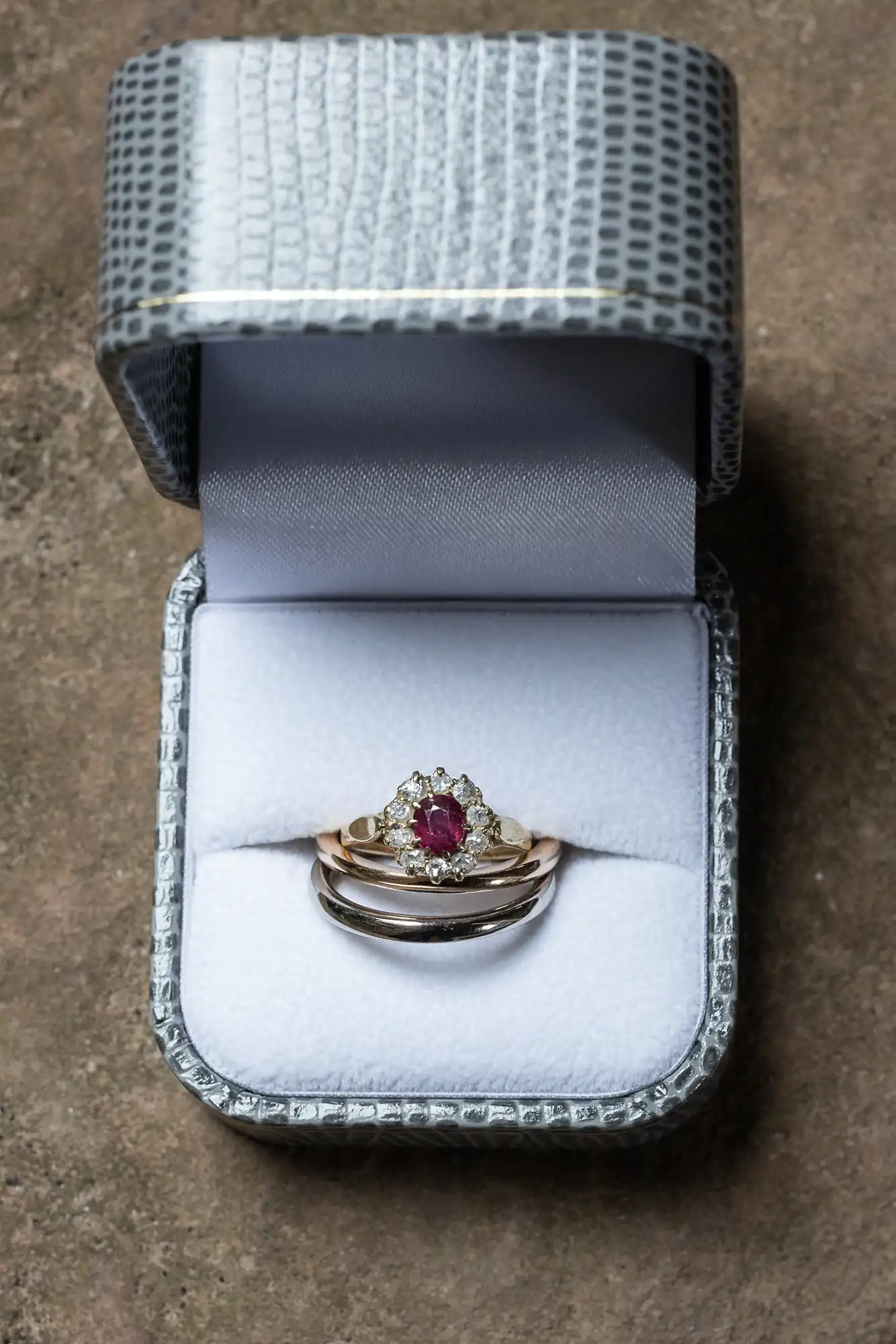 A ring with a red gemstone and small diamonds in a silver and white ring box with a textured lid.