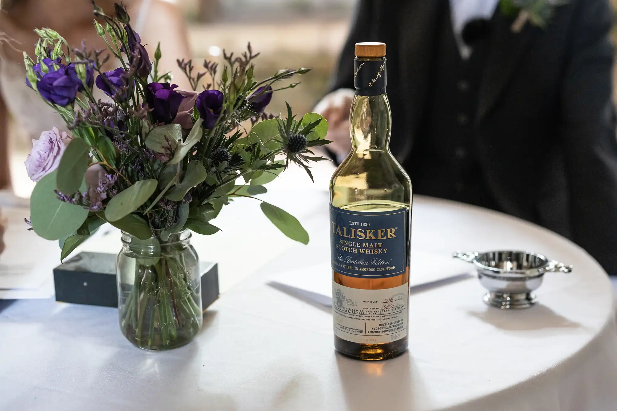 A bottle of Talisker single malt Scotch whiskey next to a vase of purple and green flowers on a round table.