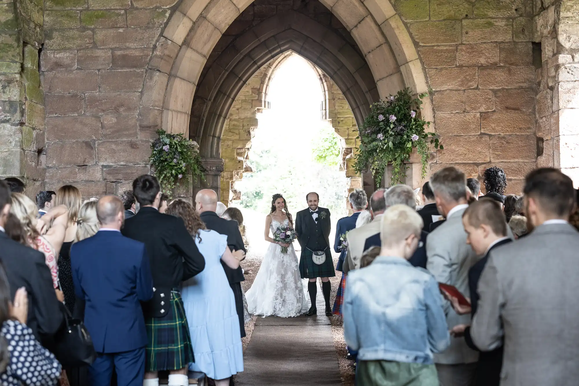 A bride and groom walk down the aisle in an archway, while guests stand on either side, celebrating their wedding.