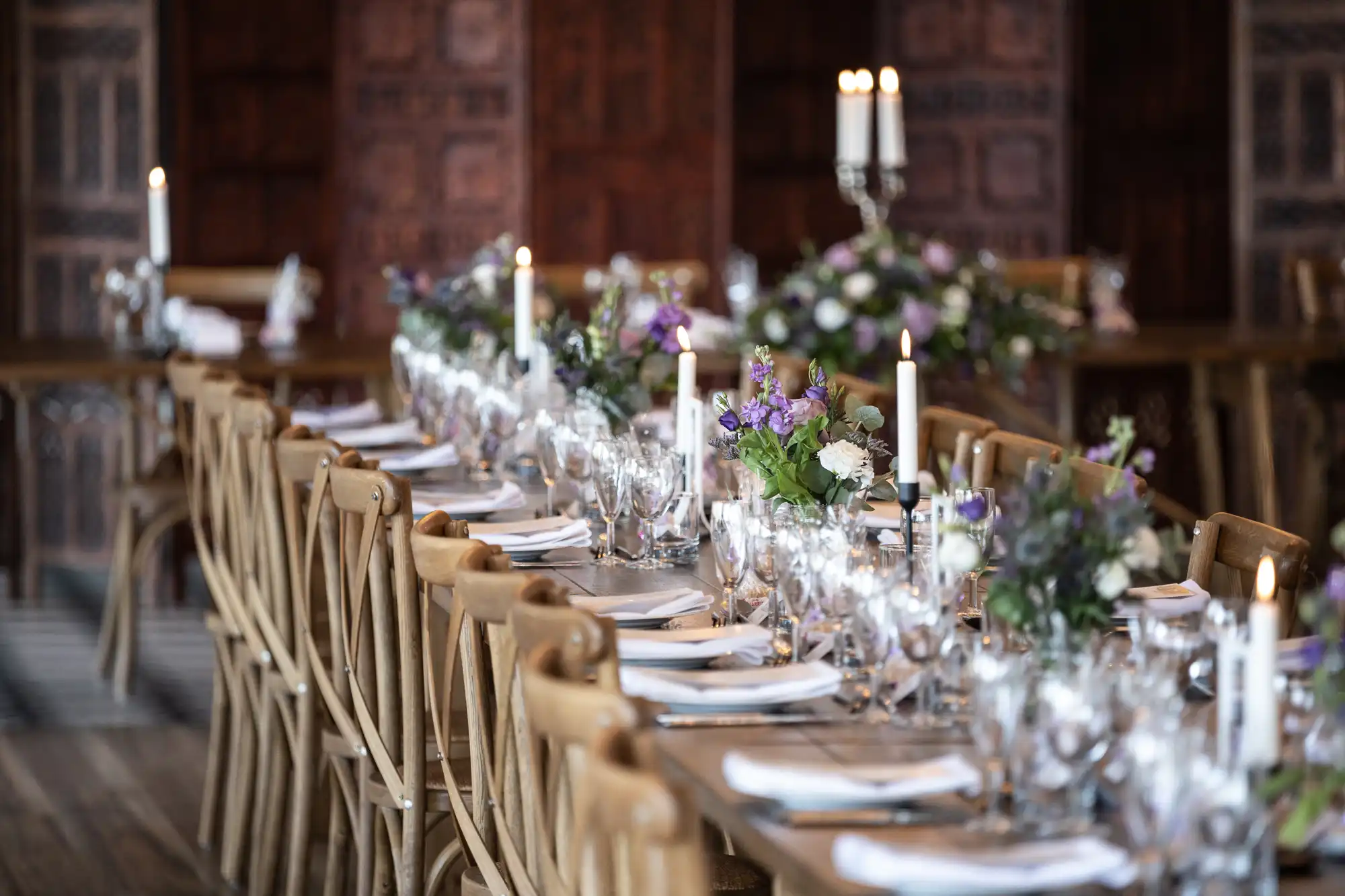 A long dining table is set for a formal event with candles, glasses, plates, and floral centerpieces in an ornate, wood-paneled room.