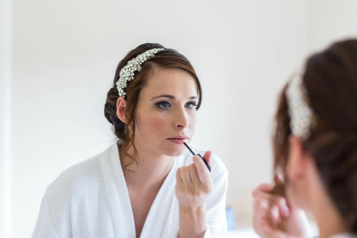 bride applies lip gloss in front of a mirror