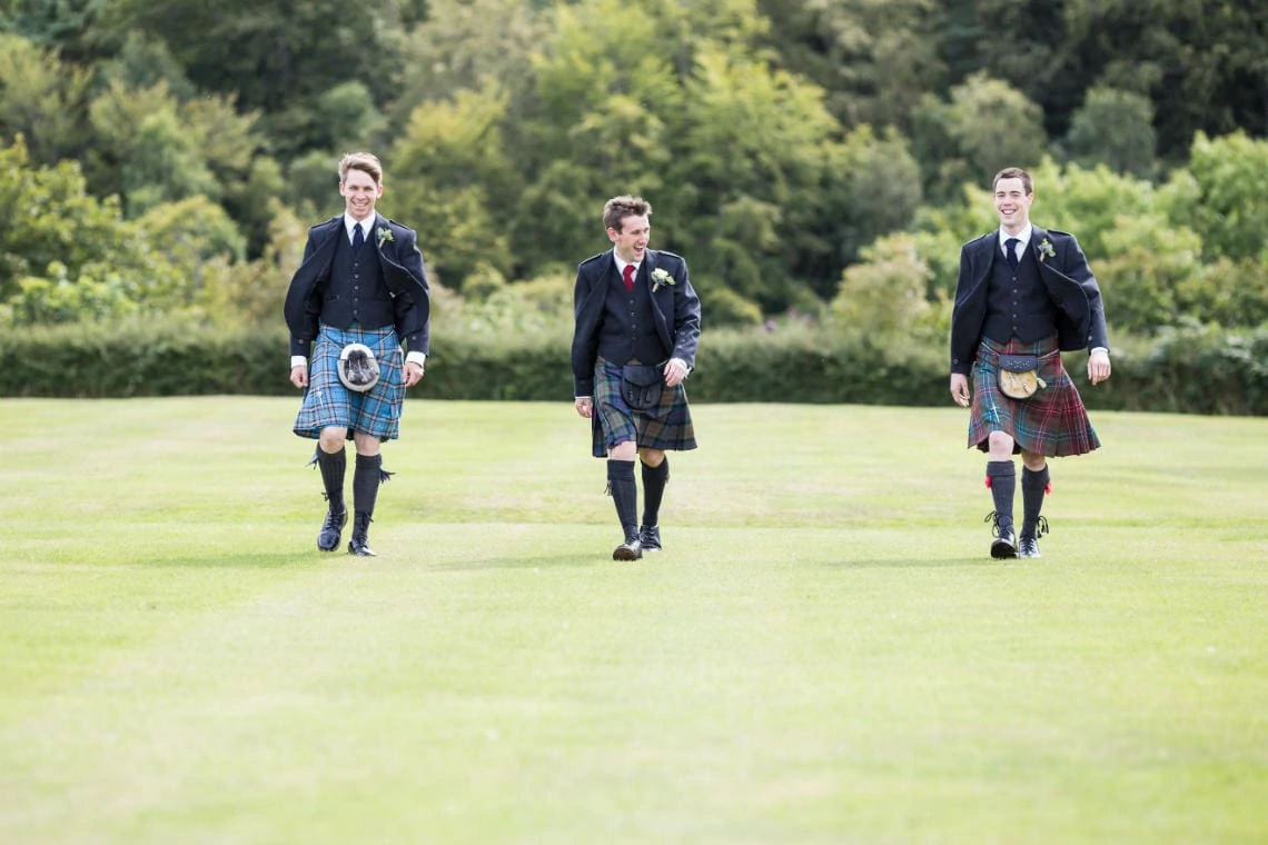 groom and the boys wearing kilts walking across the lawn