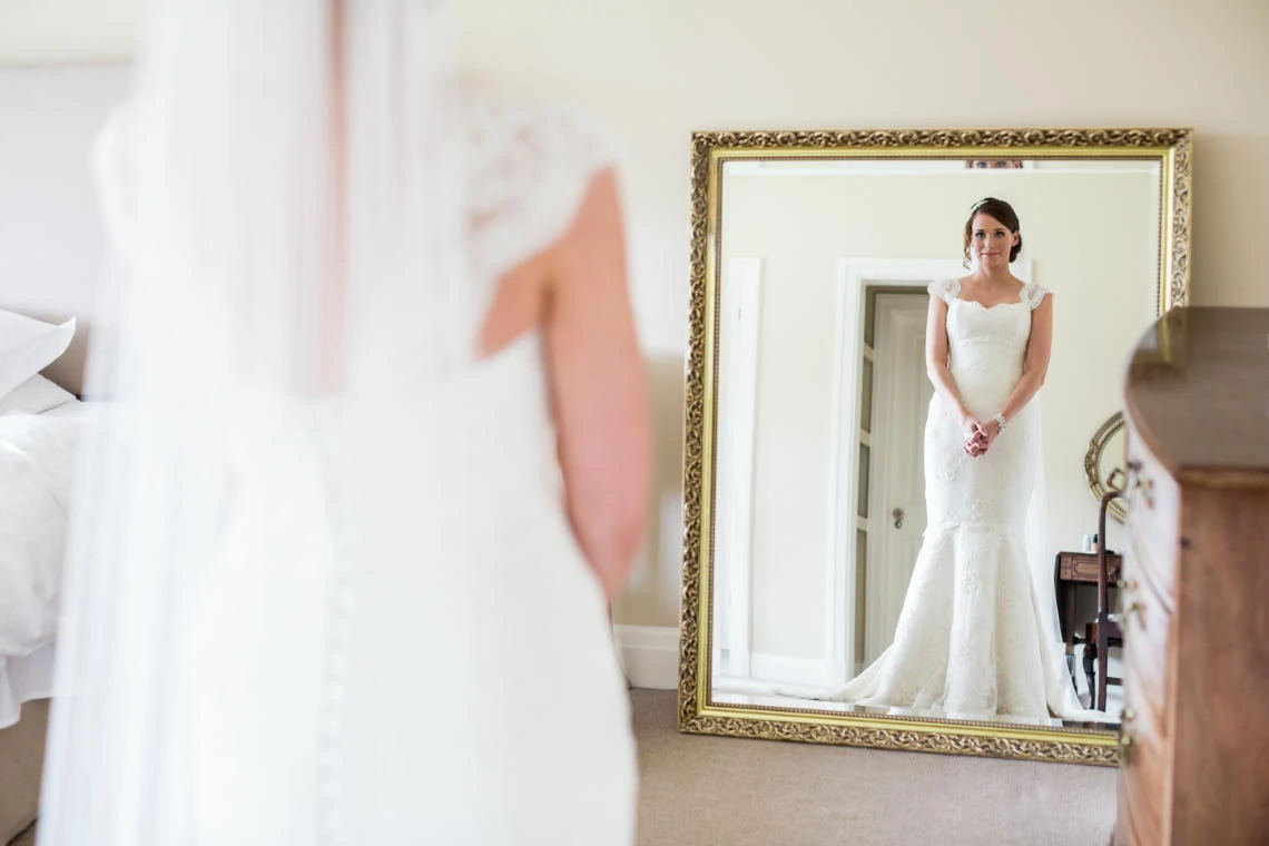 bride in her white dress standing in front of a full-length mirror