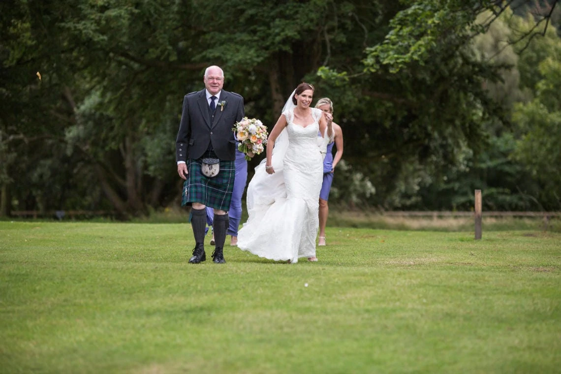 bridal party are led by the piper across the grass to the church