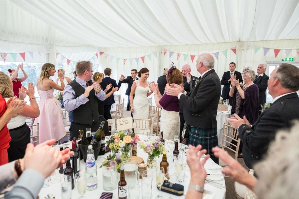 family and guests cheer and applaud the newlyweds as they make their way to the top table