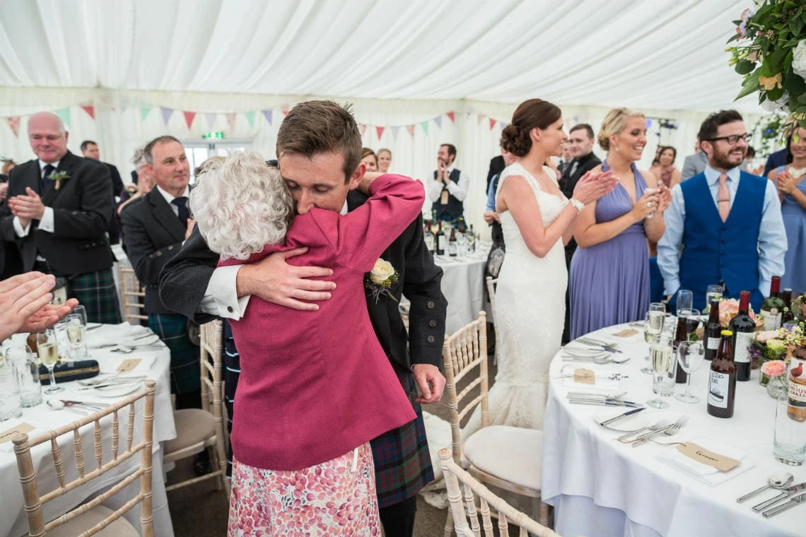 groom hugs his granny at the top table in the marquee