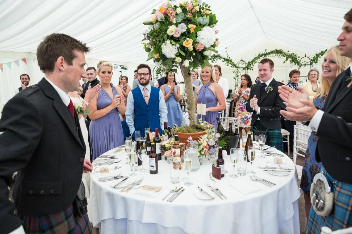 guests welcome the newlyweds to the top table in the marquee