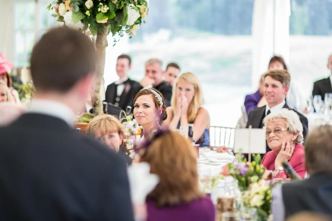 bride watching her groom delivering his speech in the marquee
