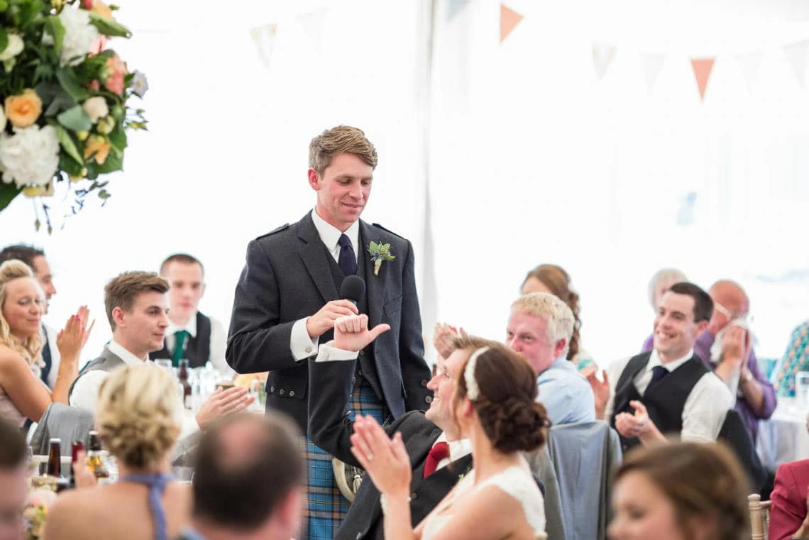 groom gives a thumbs up to his best man during the speech in the marquee