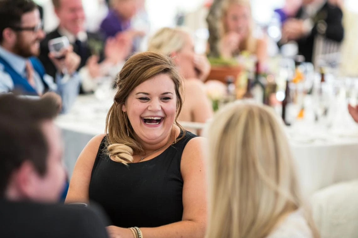 female guest laughing during the best man's speech