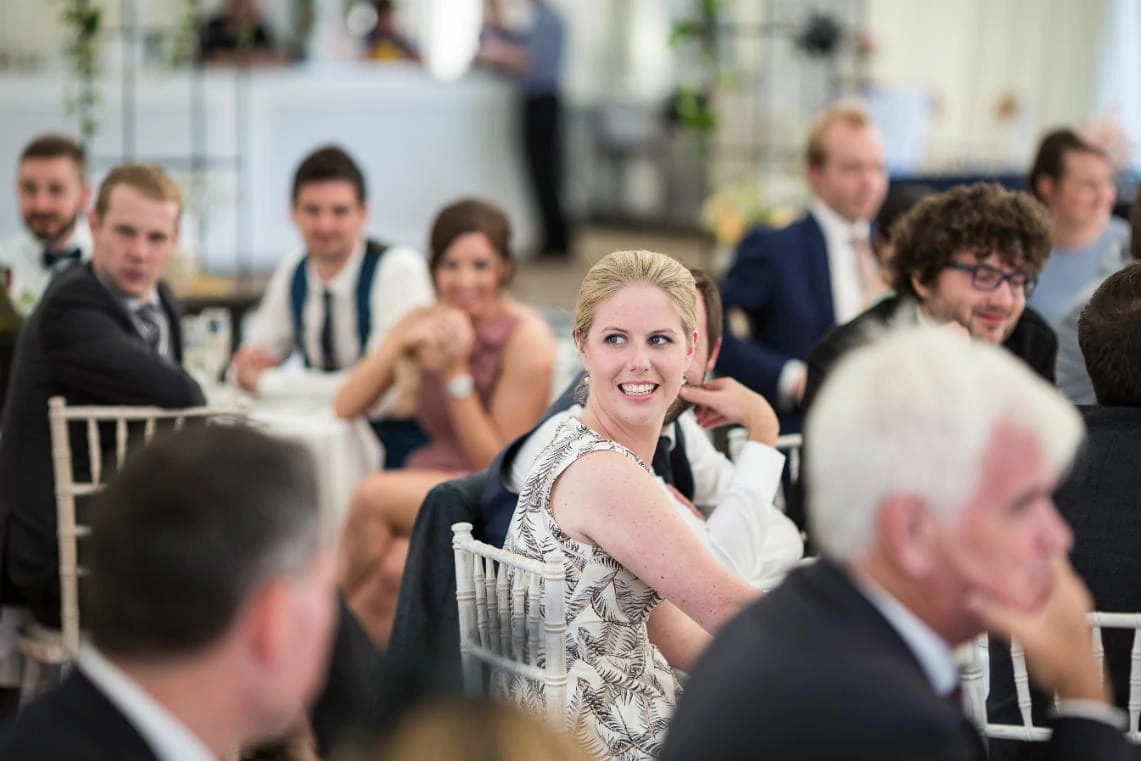 a female guest smiling as she listens to the best man's speech