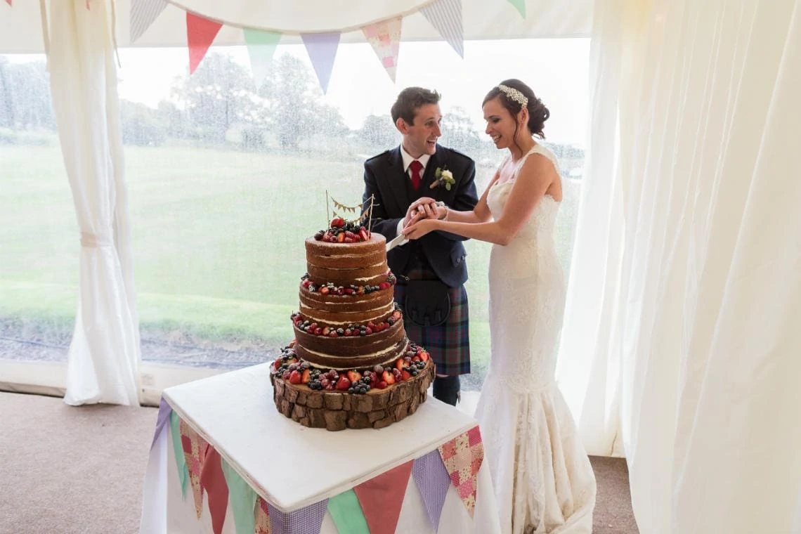 bride and groom cut their naked wedding cake in the marquee