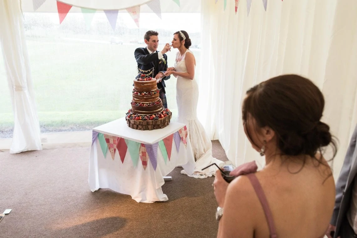 groom feeds his bride a piece of the naked cake