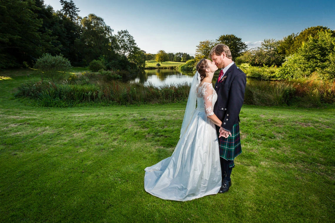 Dunglass Estate wedding Katie and Tom kiss in front of the pond