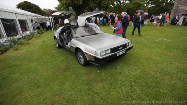 Dunglass Estate wedding videographer: A silver DeLorean car with gull-wing doors open is parked on grass at an outdoor event, surrounded by people.