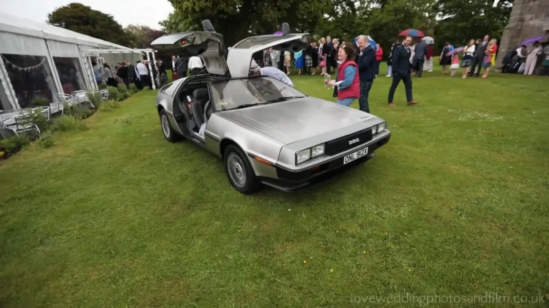 Dunglass Estate wedding videographer: A silver DeLorean car with gull-wing doors open is parked on grass at an outdoor event, surrounded by people.