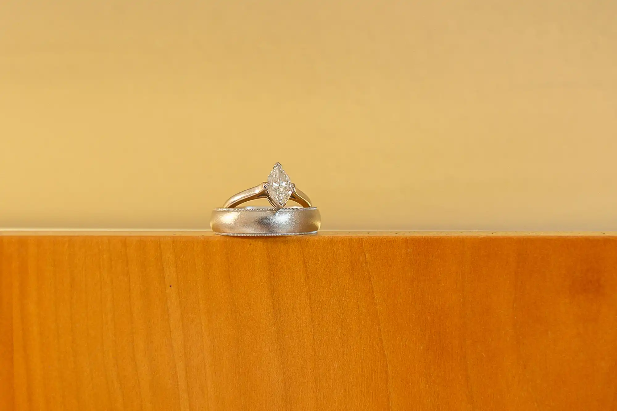 A diamond ring placed on a wooden surface against a soft yellow background.