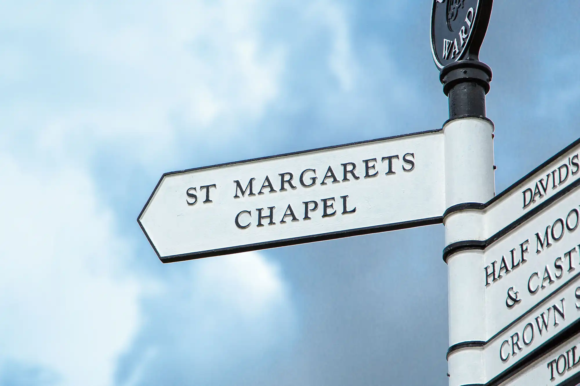 Directional signpost pointing to "st margarets chapel" against a cloudy sky.