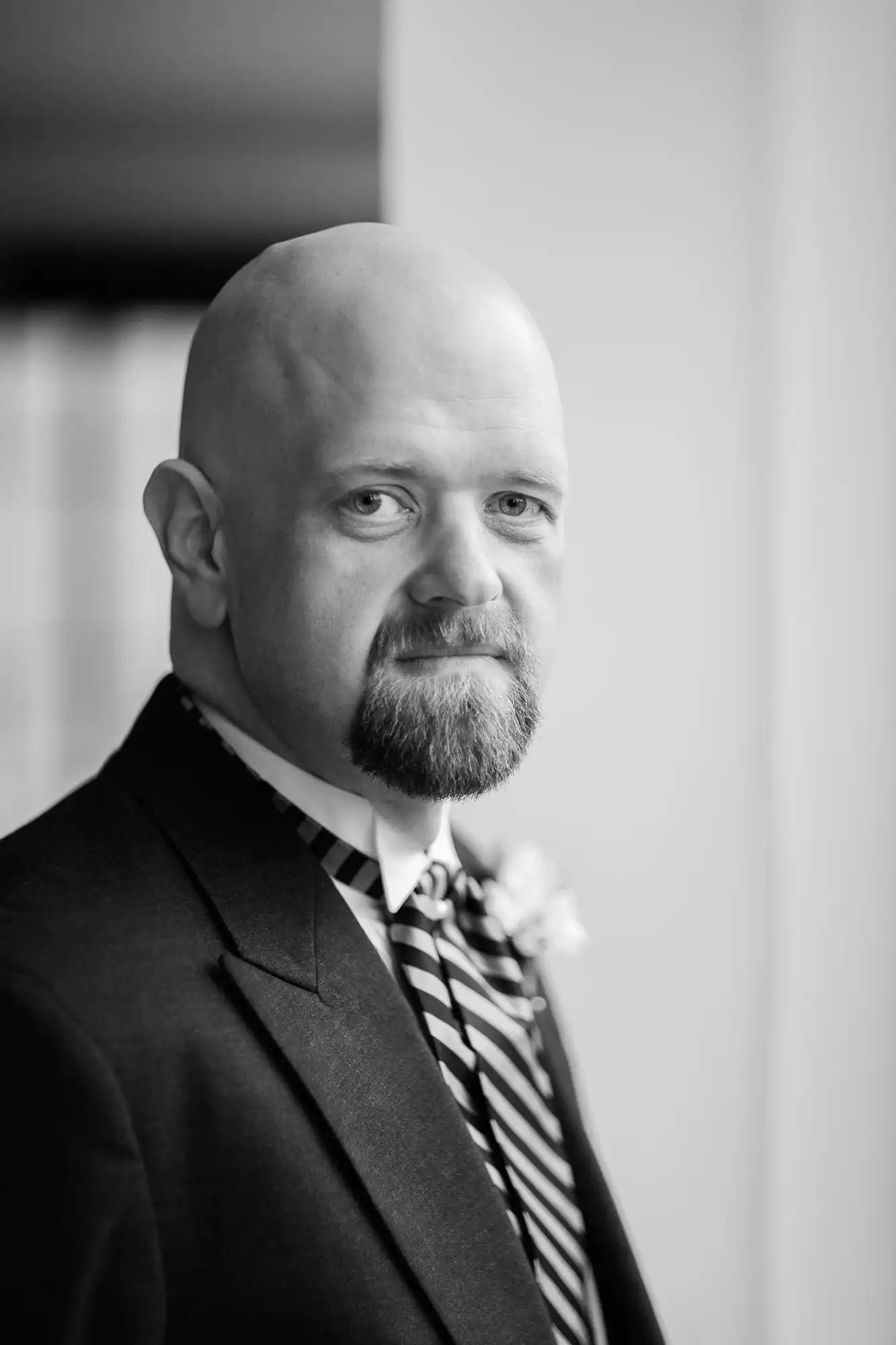 Black and white portrait of a bald man with a beard, wearing a suit and striped tie, looking directly at the camera.