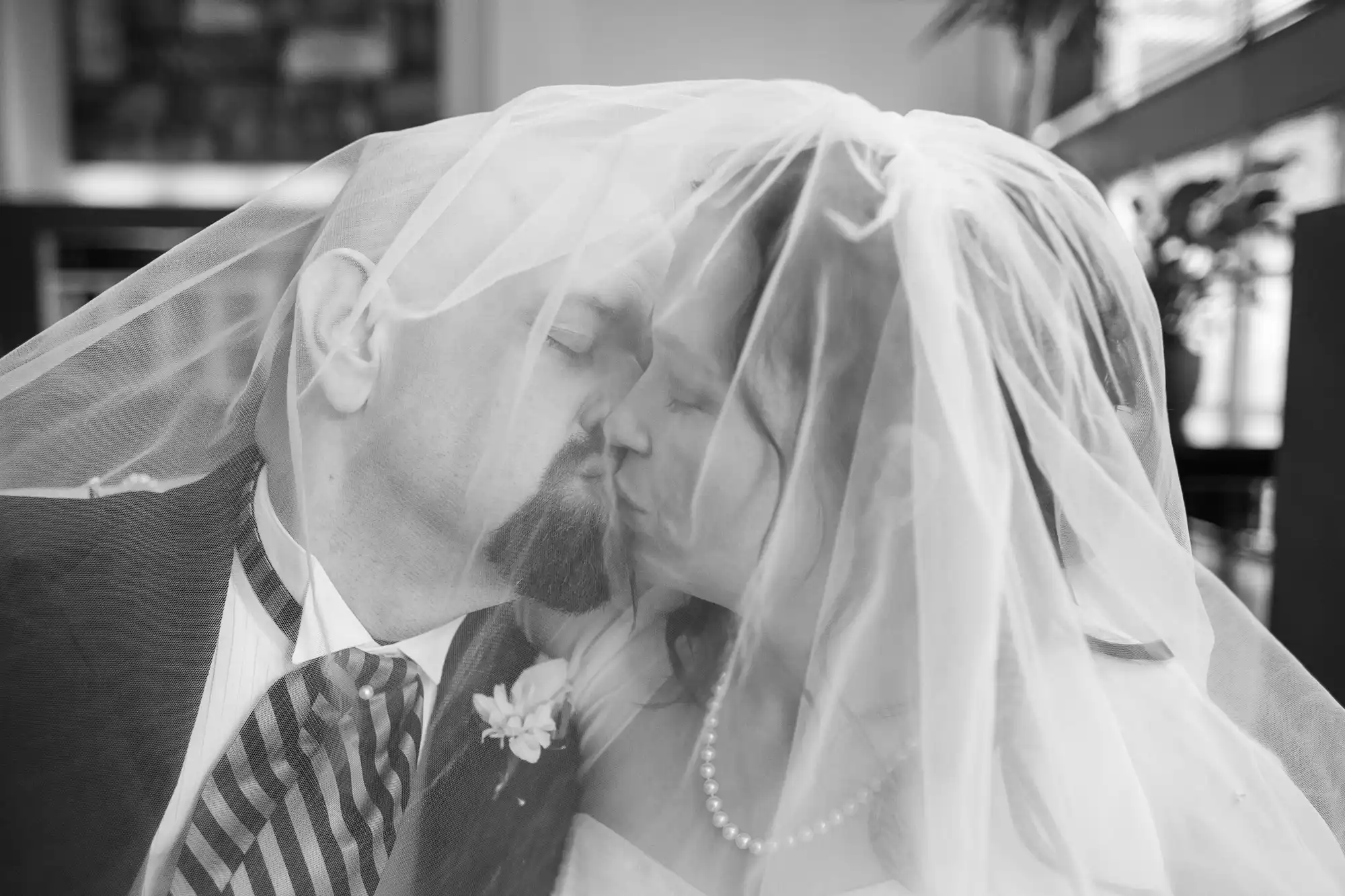 A black and white photo of a bride and groom kissing under a veil.
