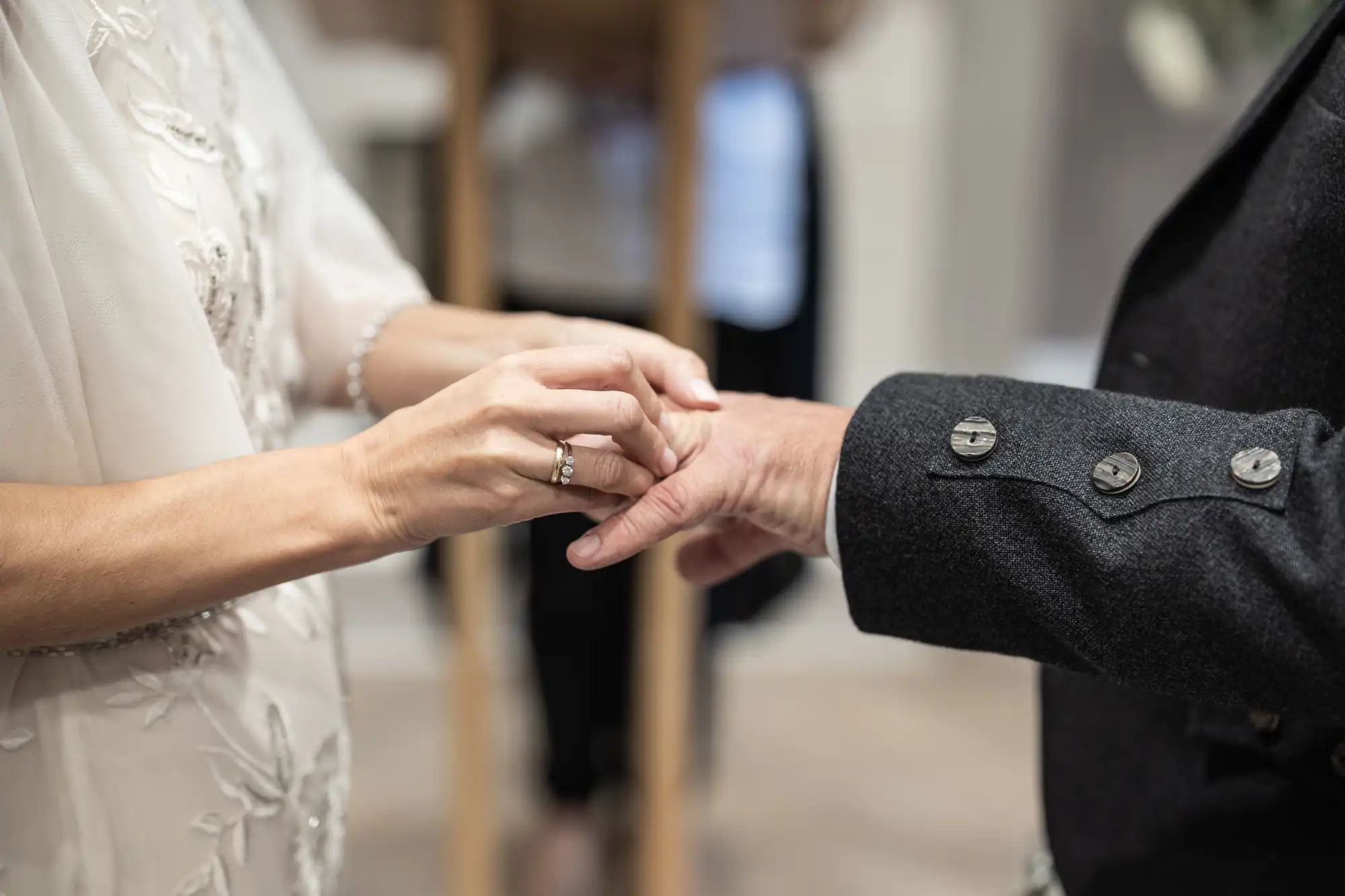 Close-up of a person placing a ring on another person's finger in a wedding ceremony setting.