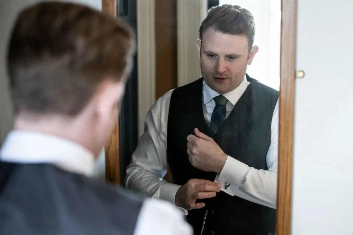 Groom looking in the mirror and adjusting his cufflinks