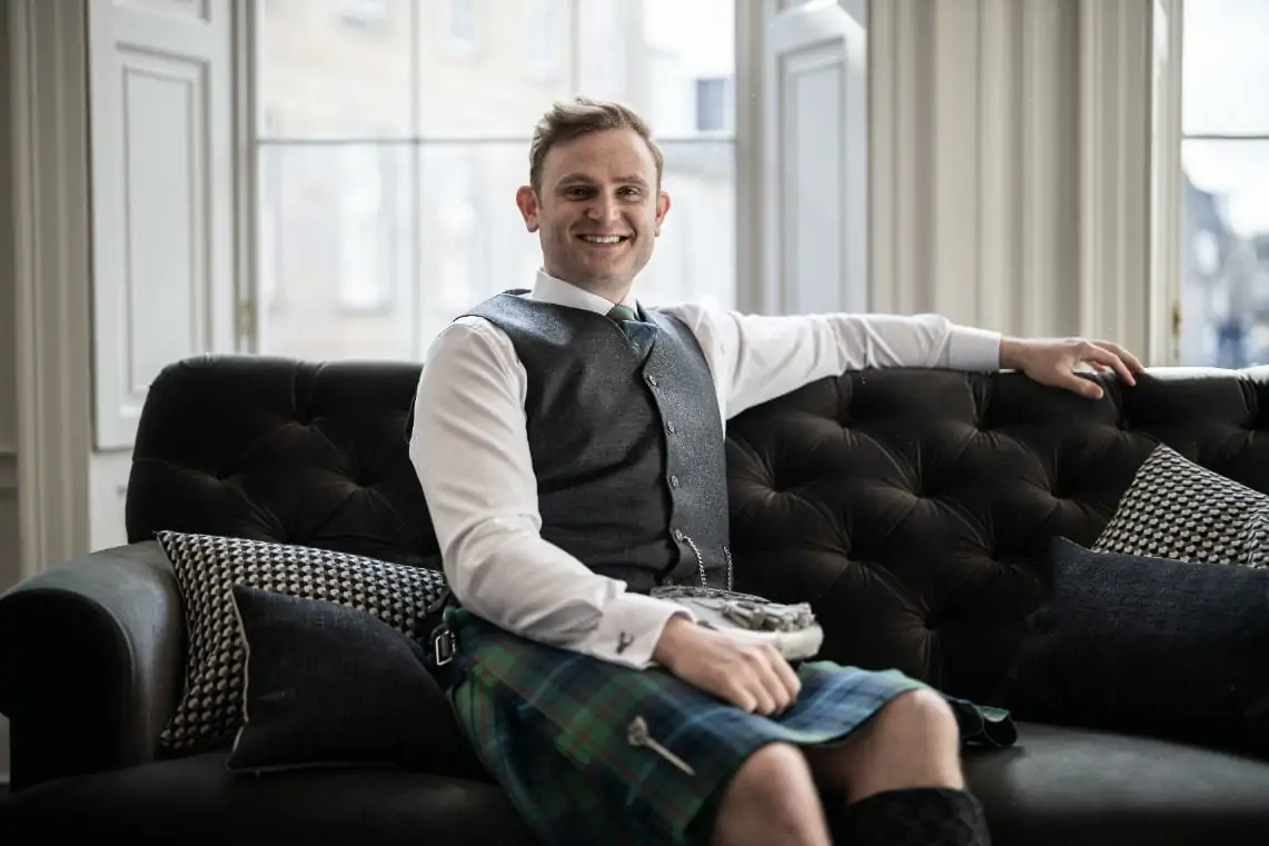 Groom dressed in highland wear sitting on sofa