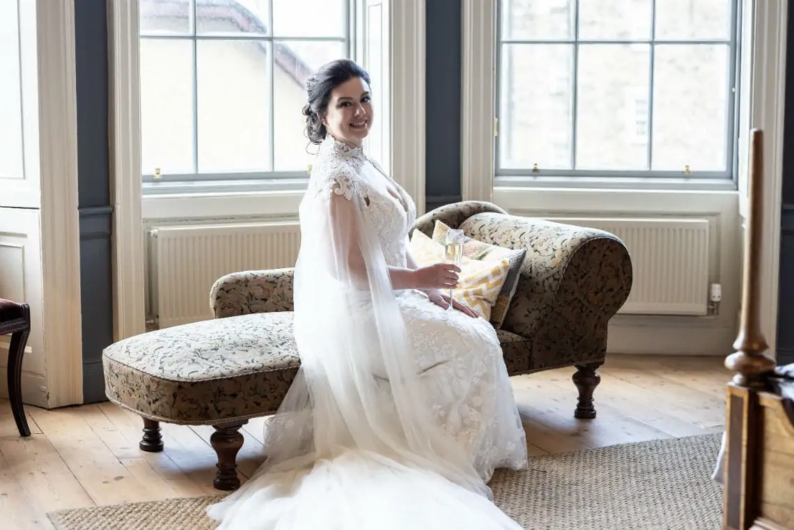 Bride sitting on chaise longue smiling into the camera