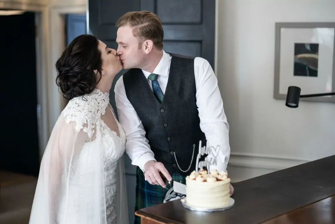Bride and Groom kissing as they cut their wedding cake
