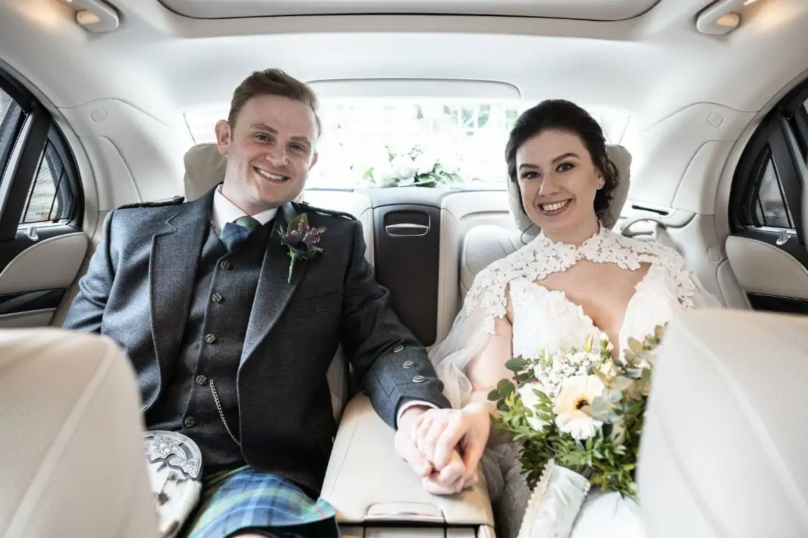 Bride and groom sat in the rear of a Mercedes wedding car