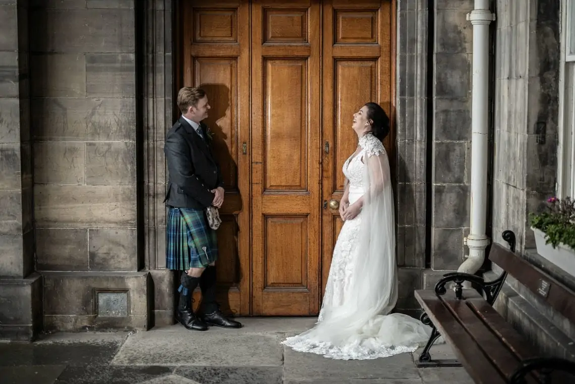 Bride and Groom looking at each other and laughing in front of wooden doors